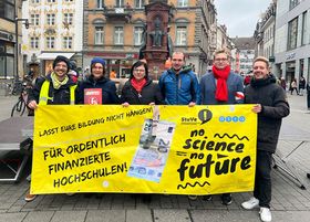 Das Bild zeigt sechs Personen, die ein gelbes Protestbanner halten