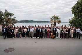 Gruppenbild der Absolvent*innen auf der Insel Mainau. Im Hintergrund ist der Bodensee zu sehen, links und rechts stehen Palmen.