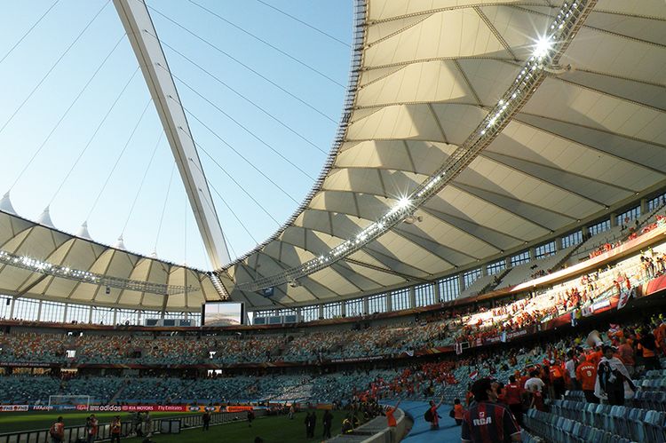 Innenansicht eines Fußballsatdions: Man sieht die Ränge, einen Teil des Spielfeldes, Fans und das Dach des Stadions.