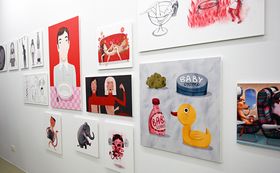 Das Bild zeigt eine weiße Wand, an der unterschiedliche bunte Illustrationen hängen.