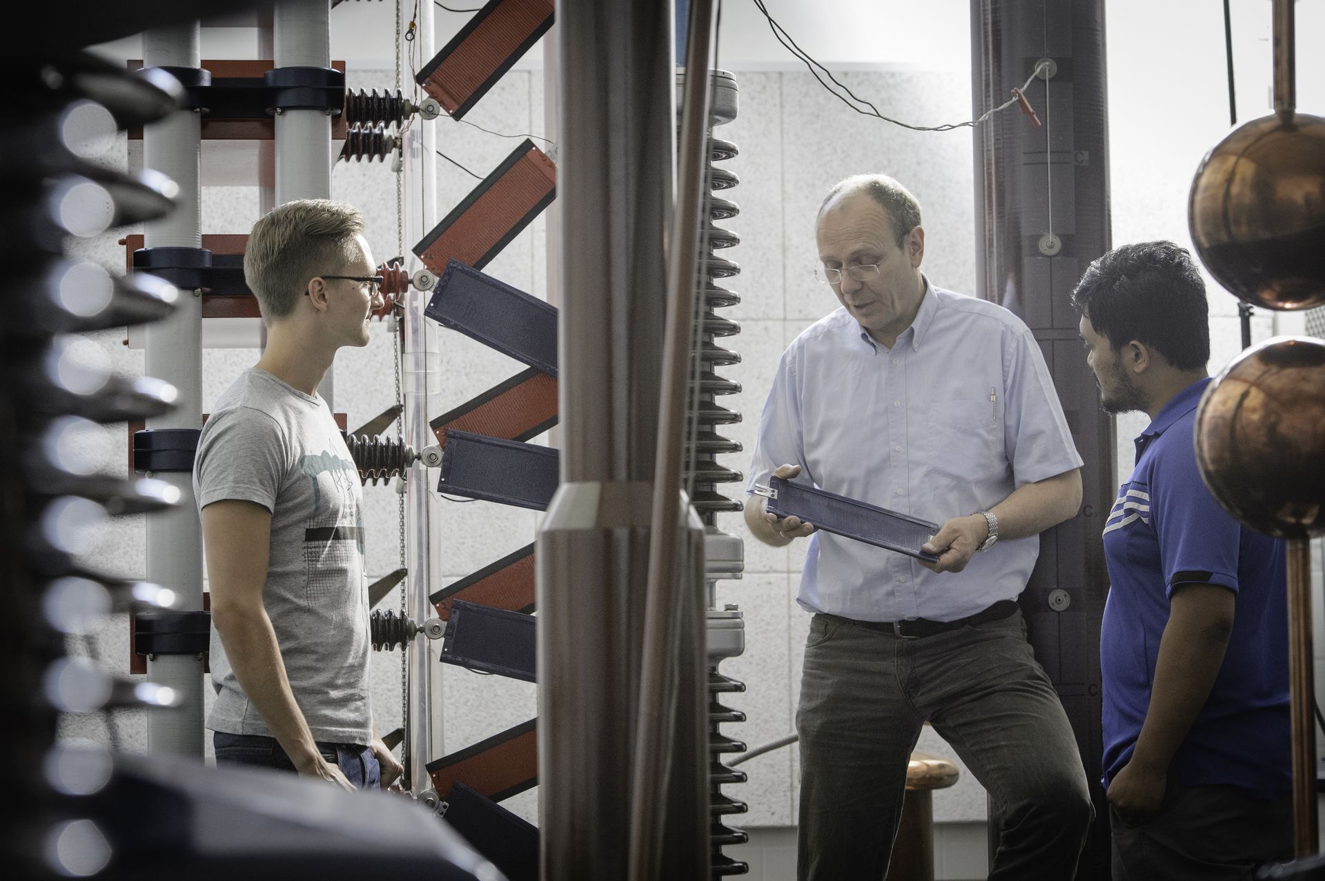 Ein Professor zeigt zwei Studierenden Bauteile einer Maschine