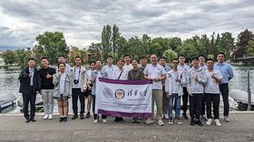 Eine große Gruppe von jungen Menschen aus China, die vor einem Fluss stehen. Sie halten eine Fahne ihrer Universität hoch. 