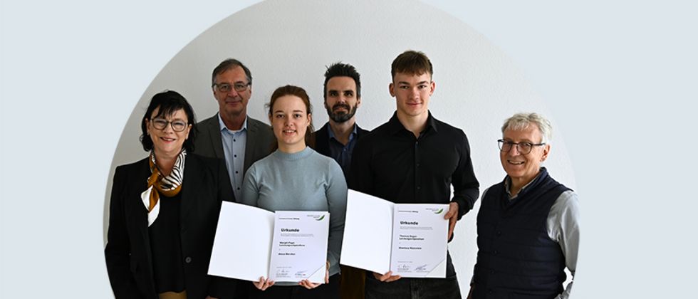 Eine sechsköpfige Gruppe Menschen. Eine junge Frau und ein junger Mann stehen in der Mitte und halten stolz ihre Stipendiumsurkunde in den Händen.