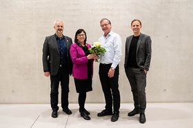 Das Präsidium lächelt. Von links nach rechts: Manfred Schnell in dunklem Anzug, Sabine Rein in schwarzem Kleid und fuchsiafarbenem Blazer, sie hält einen Blumenstrauß gemeinsam mit Thomas Birkhökzer, der neben ihr steht. Birkhölzer trägt ein weißes Hemd und schwarze Hose. Ganz rechts steht Gunnar Schubert, er trägt einen grauen Anzug und einen schwarzen Pullover.