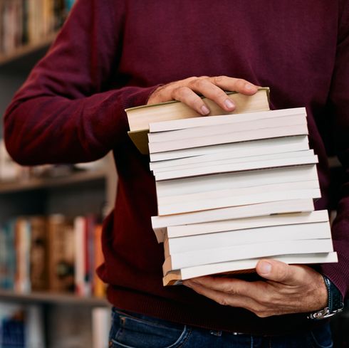 Ein Bücherstapel wird getragen von einem jungen Mann. Anonymer Ausschnitt.
