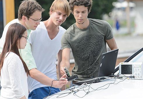 Studierende und Professor Lang arbeiten am Laptop, der auf der Motorhaube eines Audis steht. 