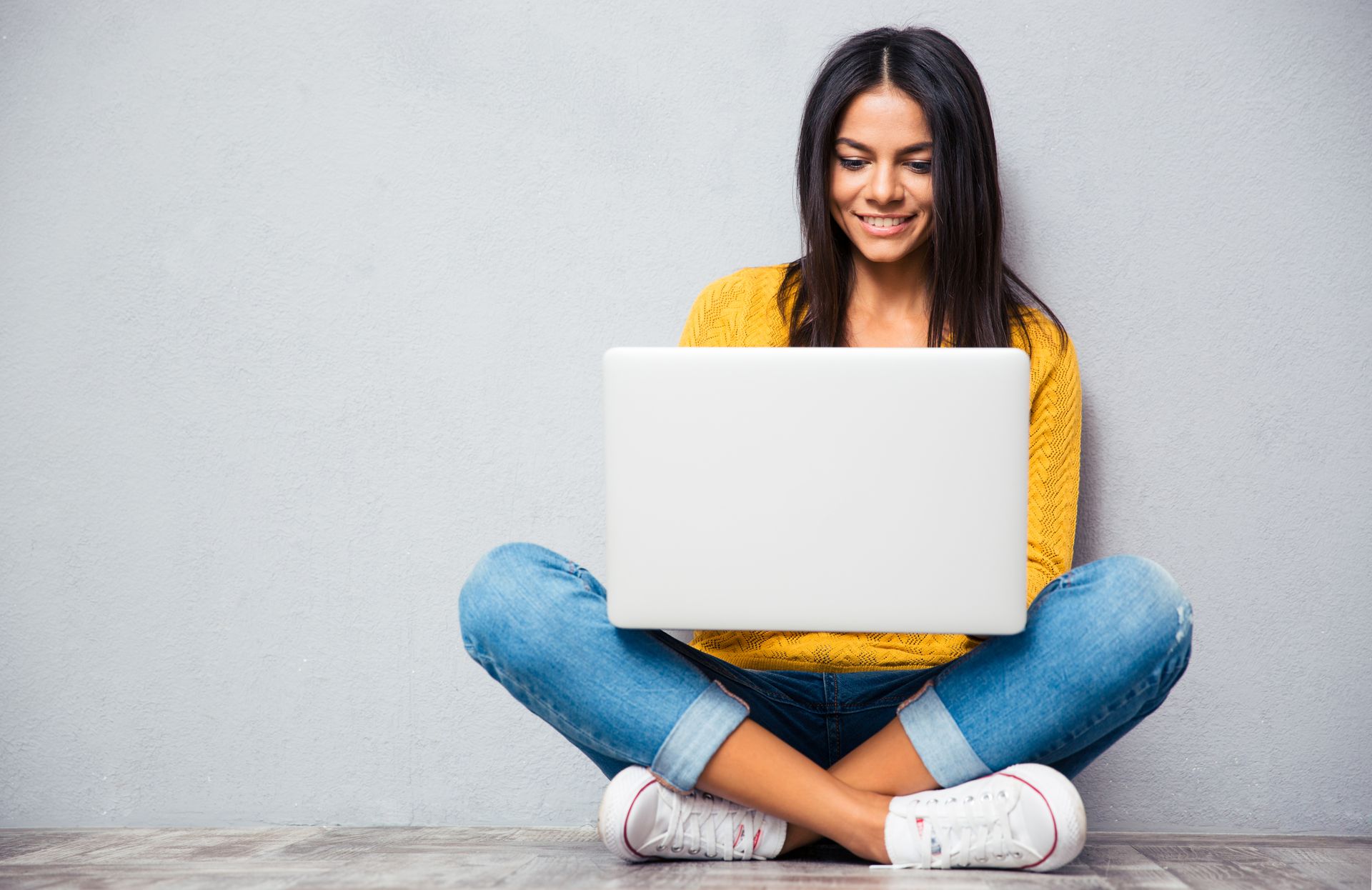 Eine junge Frau sitzt auf dem Boden und hat ihren Laptop auf dem Schoß.