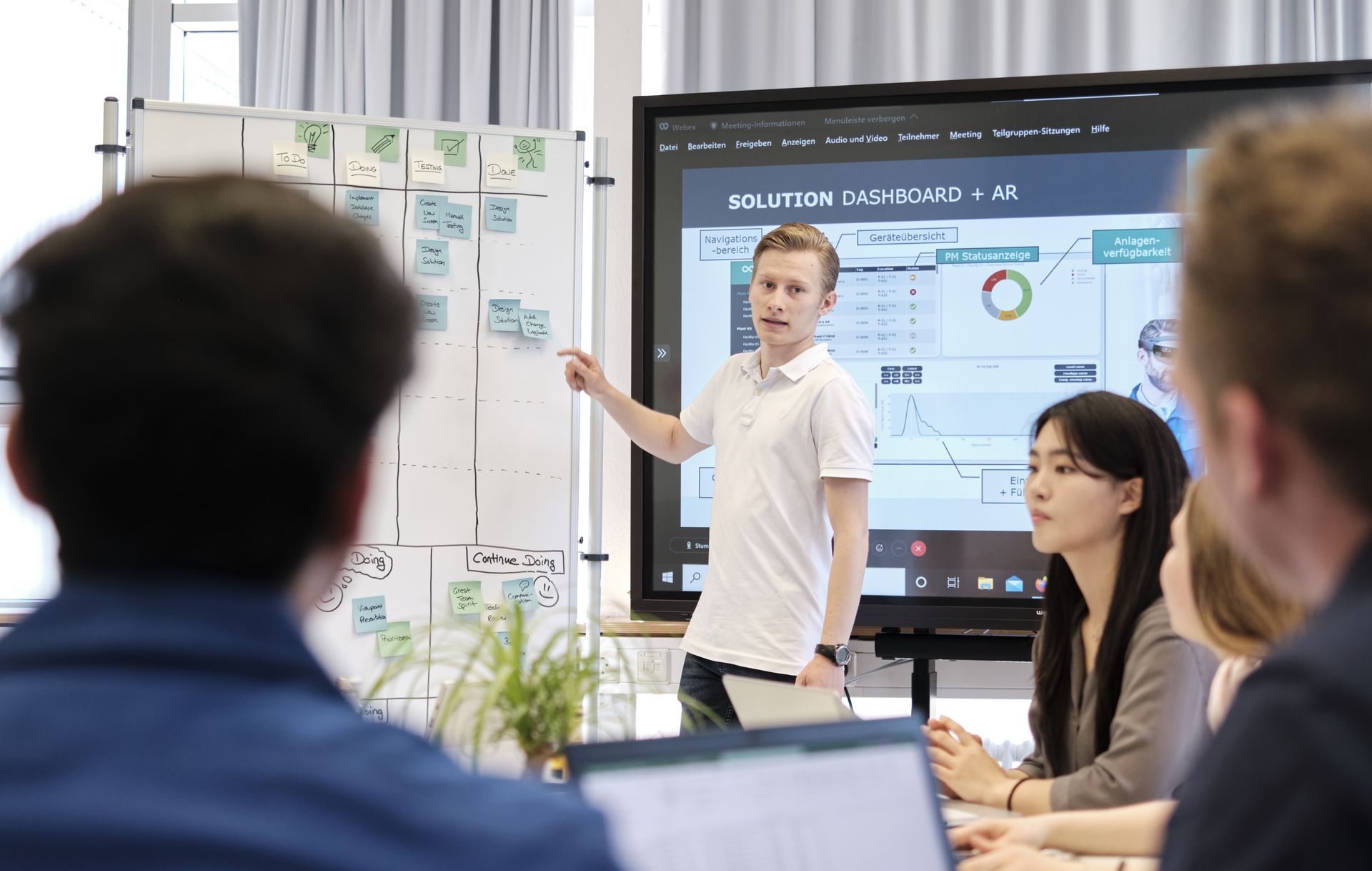 Ein Student steht vor einer Kanban-Tafel und erklärt anderen Studierenden etwas.