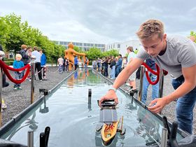 Ein Solarboot, gebaut aus einer Nussschale, wird von einem blonden Jungen in die Wasserrennbahn gesetzt