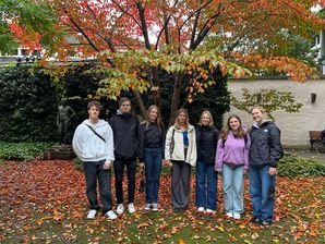 Gruppe Studierender vor herbstlich verfärbten Büschen und Bäumen