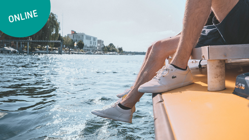 Ein Student fährt mit einem Boot im Rhein und lässt die Beine über den Rand des Bootes baumeln