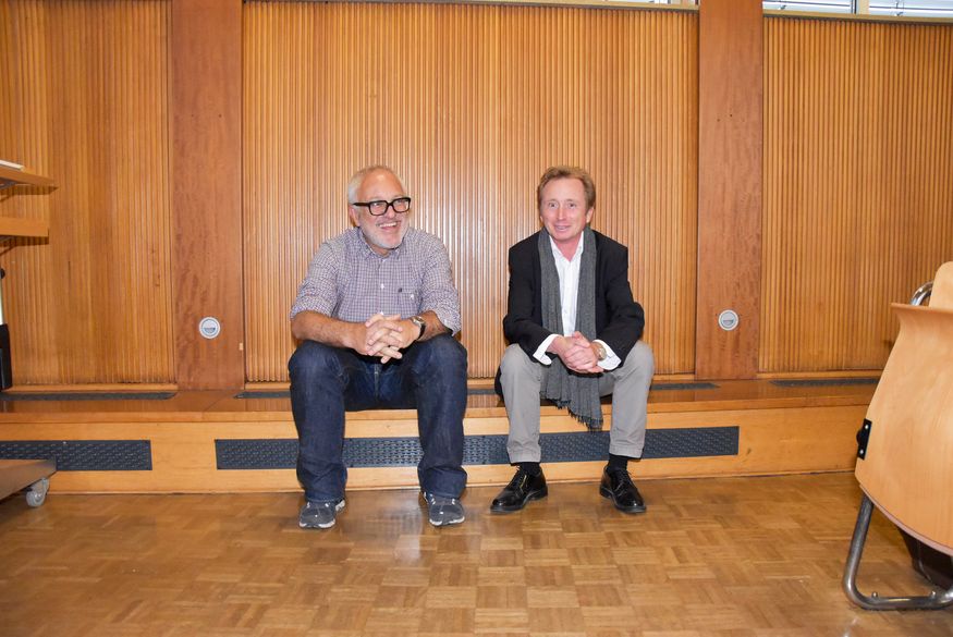 Patrick Gmür (links) und Prof. Dominik Fiederling sitzen nebeneinander vor einer holzvertäfelten Wand auf einer Holzbank.