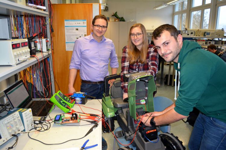 Drei Studierende arbeiten an einem Kinderfahrzeug in Form eines Traktors, das elektroonisch angetrieben wird.