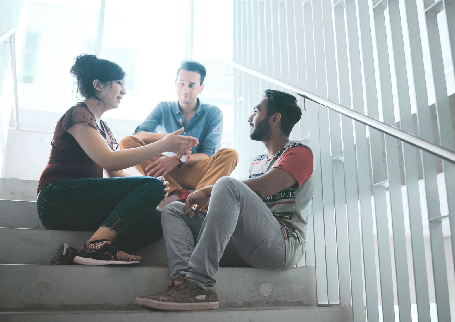 Auf einer Treppe in der Hochschule sitzen drei Studierende und unterhalten sich