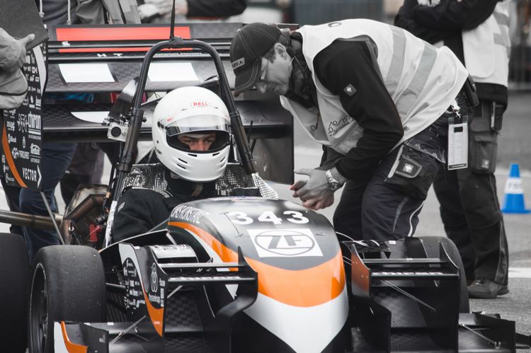 Ein Mechaniker beugt sich über einen Rennwagen, in dem ein Rennfahrer mit Helm sitzt.