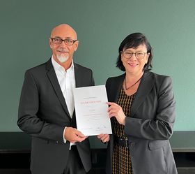 Ein Mann und eine Frau halten gemeinsam eine Dankesurkunde in den Händen und lächeln in die Kamera.