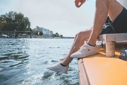 Anoynmer Ausschnitt. Ein Studierender sitzt am Seerhein, lässt sein Bein über dem Wasser schaukeln.