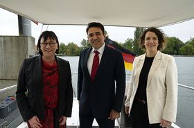 Das Bild zeigt Sabine Rein, Mohit Yadav und Lina Seitzl auf dem Forschungsboot Solgenia. Im Hintergrund ist der Seerhein sowie die Deutschlandfahne, die das Schiff trägt, zu sehen.