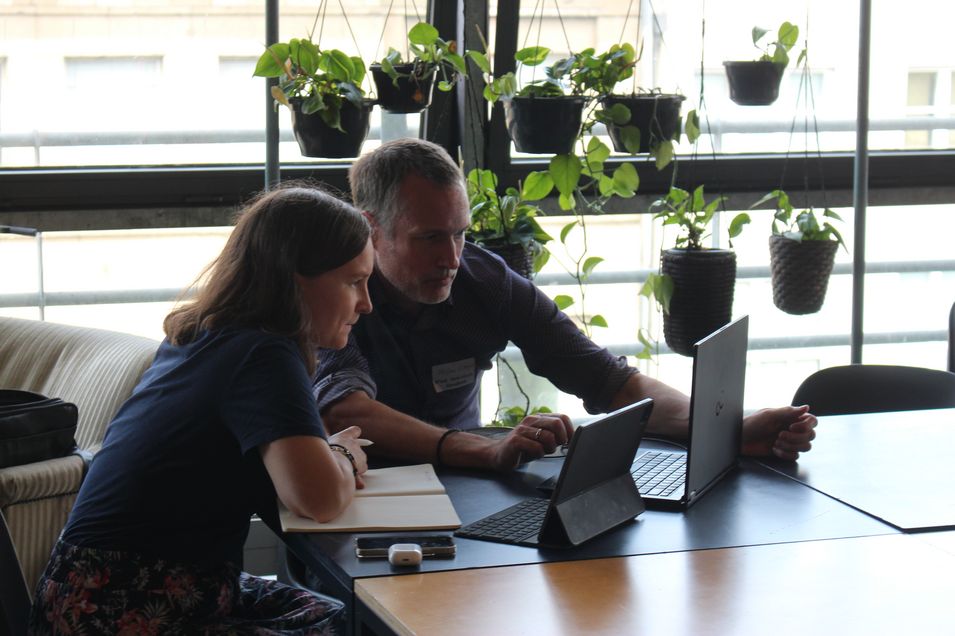 HTWG Transformationslaborförderung Stefan Stieglat und Maria-Xenia Hardt sitzen an einem Arbeitstisch. Vor ihnen stehen zwei Laptops. Sie schauen sich gemeinsam etwas auf dem Screen an und tauchen sich darüber aus.