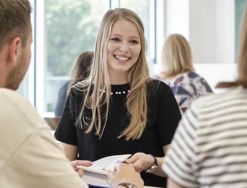 A smiling student with two fellow students during group work. Photo Credit: Philipp Uricher.