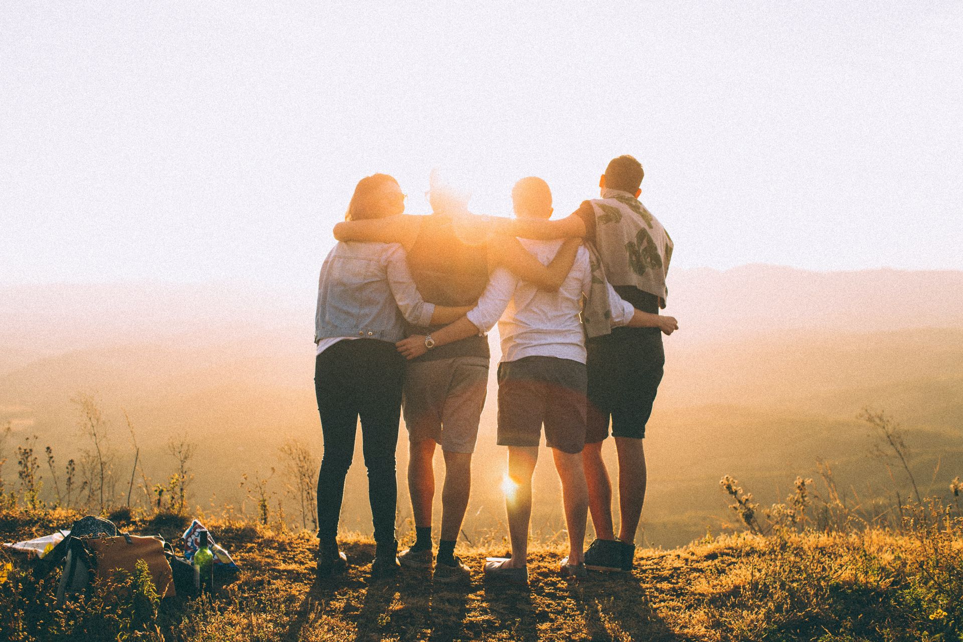 Eine Gruppe junger Menschen stehen in der Natur und blicken auf den Sonnenuntergang