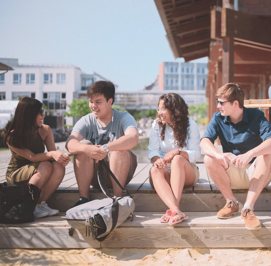 Eine Gruppe Studierender sitzen in der Sonne an der Strandbar