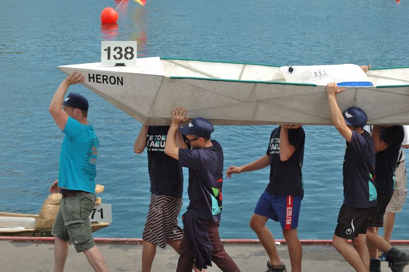 6 Personen tragen ein Betonkanu am Wasser entlang, sie sind Studenten an der HTWG Konstanz und Teil des Betonkanu Teams