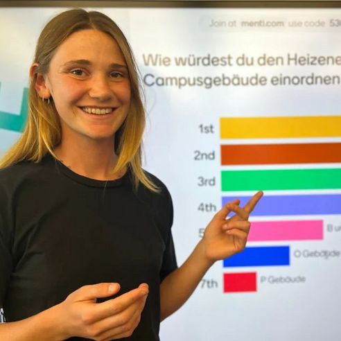 Die Klimaschutzmanagerin Mirjam Gröger steht vor einer Infografik zum Wärmeenergiebedarf der Hochschule