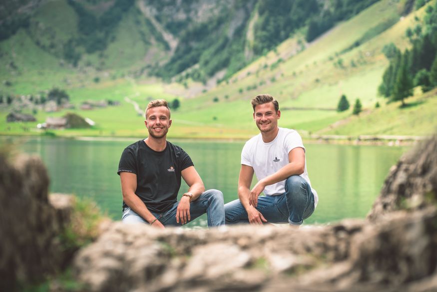 Alexander Sack und Markus Schaffner kniend vor einem Bergsee in den Alpen. Sie tragen die "Touch of Alps"-T-Shirts.