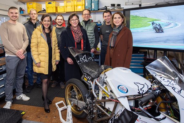 Eine Gruppe von Studierenden, Lehrenden und Politikerinnen steht hinter dem Elektro-Rennmotorrad und blickt in die Kamera.