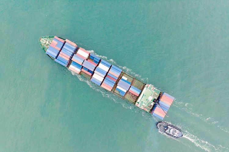 Luftaufnahme eines Containerschiffes mit Begleitboot.