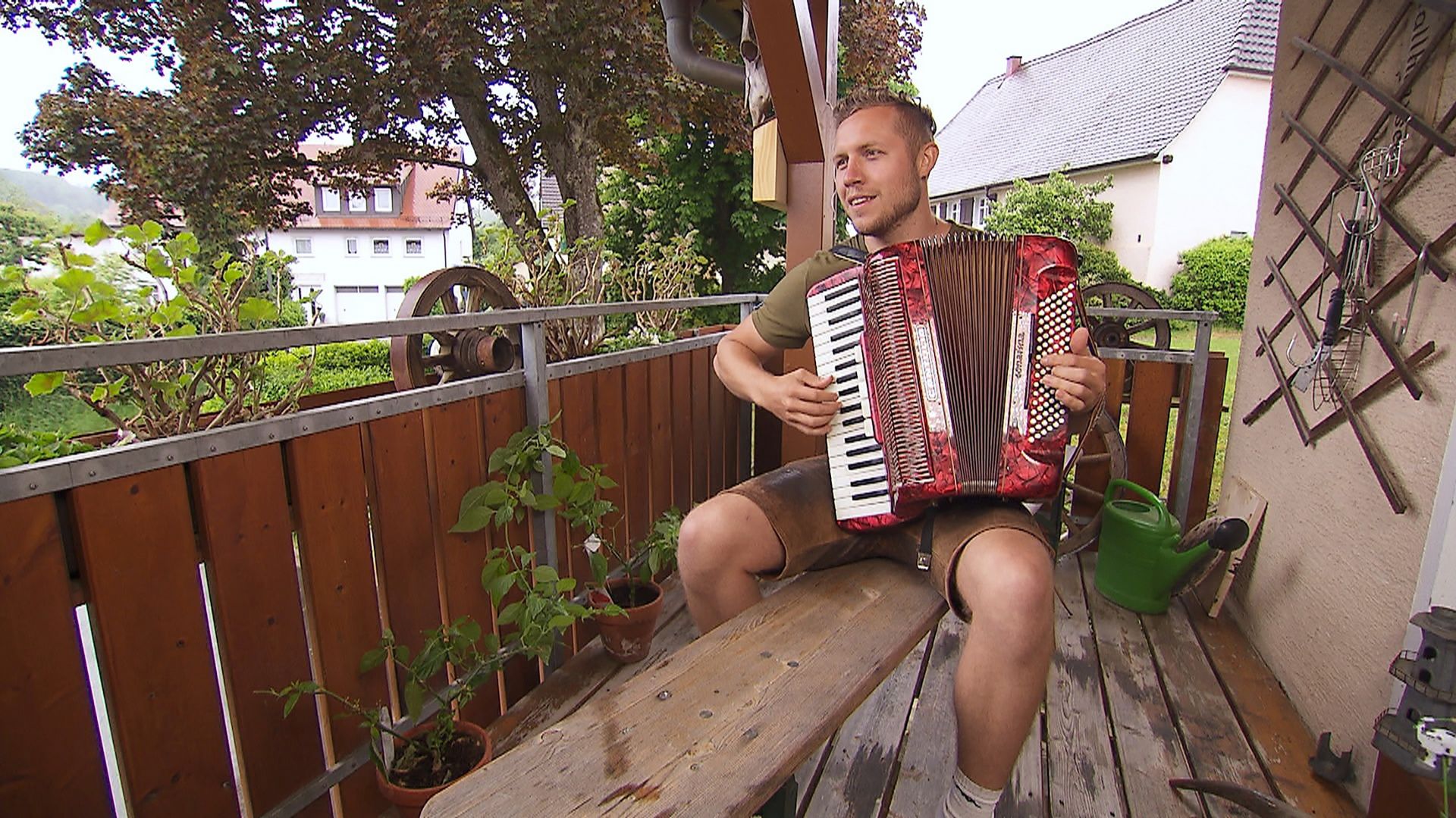 Patrick Romer sitzend auf einer Bierbank auf dem Balkon. Er spielt Akkordeon.