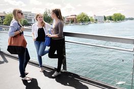 3 Studentinnen unterhalten sich auf Fahrradbrücke, Seerhein und HTWG-Campus im Hintergrund
