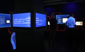 Blau leuchtende Bildschirme in einem verdunkelten Raum mit schwarzen Wänden in der Ausstellung "LINK - zur künstlichen Intelligenz"