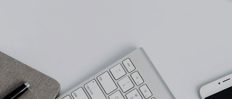 Eine Tastatur, ein Smartphone und ein Notizbuch von oben fotografiert. Sie ragen vom unteren Bildrand ins Bild und sind nur teilweise zu sehen.