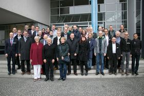 Eine große Gruppe von Menschen in Geschäftskleidung posiert vor einem Gebäude auf dem HTWG-Campus fürs Foto.