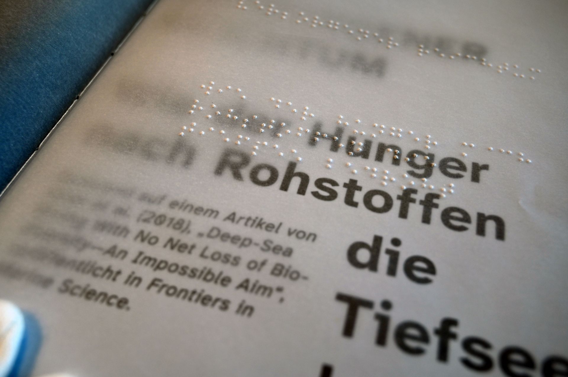 Transparente Magazinseite mit Braille-Schrift, Blick auf darunter liegende Seite in normaler Schrift