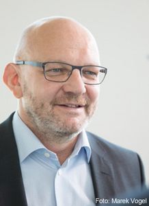 Professor Stephan Grüninger mit eckiger Brille, grauen Anzug und blauen leicht geöffneten Hemd.