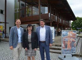 Drei schick gekleidete Personen (2 Männer und eine Frau) stehen vor einem Gebäude