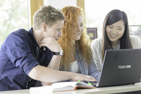 Drei Studierende lernen zusammen und schauen interessiert, lächelnd in ein Notebook
