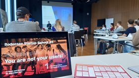 Ein Saal voller Teilnehmer*innen der Bodensee Startup School, die dem Vortragenden vor der grossen Leinwand lauschen.