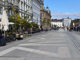 Ein breiter, frisch gepflasterter Bahnhofsplatz. Links sind Ausschnitte eines Cafés zu sehen. 