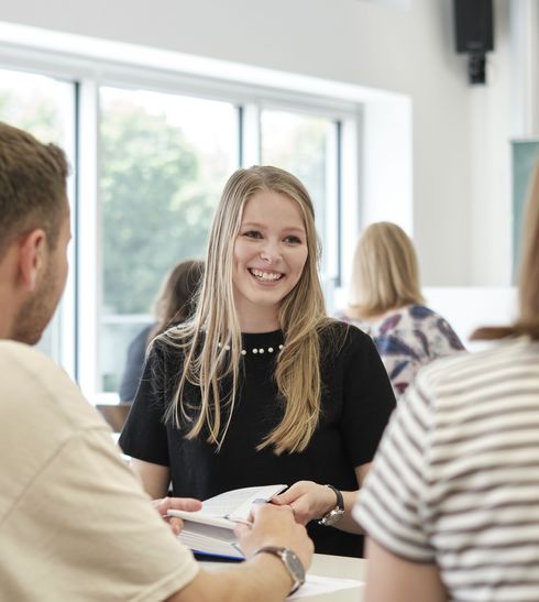 Eine Studentin, die lächelt, mit zwei KommilitonInnen bei der Gruppenarbeit.