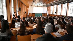 In einer Aula sitzen viele junge Menschen 