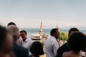 Eine Personengruppe steht auf einer Dachterrasse mit Blick auf den Bodensee und die Imperia Statue