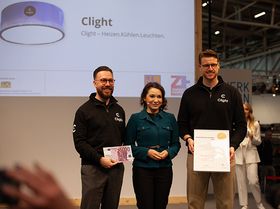 Ein Mann, eine Frau und ein weiterer Mann stehen auf einer Bühne und lächeln in die Kamera 