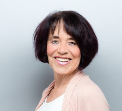 Annette_Kleinfeld_2019 Sie trägt einen kurzen, schwarzen Bob, ein weißes Oberteil mit einer rosa Jacke und blickt nach vorne.