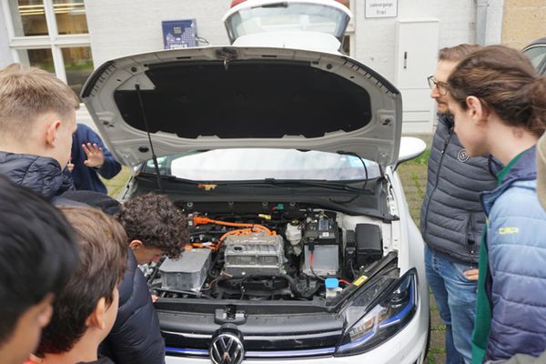 Eine Gruppe junger Menschen steht vor dem geöffneten Motorraum eines E-Autos und blickt hinein.