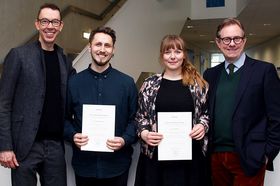 Vier Personen posieren fürs Foto. Die beiden in der Mitte halten Urkunden in den Händen.