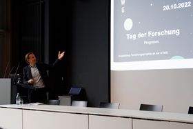 Prof. Dr. Gunnar Schubert steht an einem Rednerpult und weist mit dem linken Arm auf eine Präsentation.